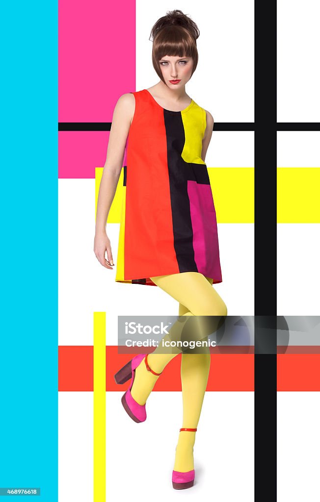 Model In Bright Retro Colors Colorful concept in sixties retro fashion style with Caucasian model posing full body over designed background with colorful bright stripes and color blocks. 1960-1969 Stock Photo