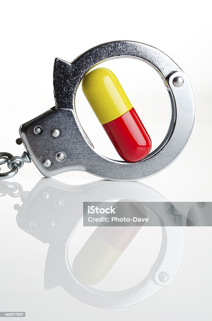 High cost of illegal drugs Pills and handcuffs together on a white tabletop Capsule - Medicine Stock Photo