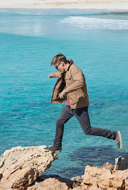 istock Young man bounds along coastline rocks 468983922