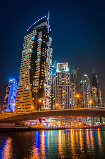 The high rise hotels and luxury apartment blocks, construction cranes and shopping malls of the Dubai Marina illuminated against the blue dusk sky reflecting in the tranquil waters below. ProPhoto RGB profile for maximum color fidelity and gamut.