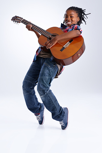 A happy young African-American boy playing a guitar while balancing on his toes