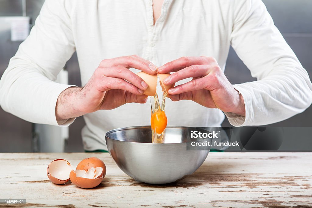 Cook breaking an egg in to the bowl Close up shot of a men breaking an egg into a metal bowl in the kitchen Animal Shell Stock Photo