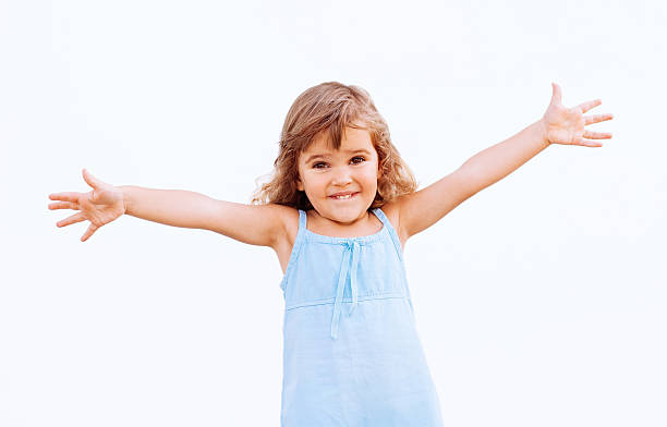 Smiling young girl in a blue dress with arms outstretched Funny little girl with arms outstretched arms outstretched stock pictures, royalty-free photos & images