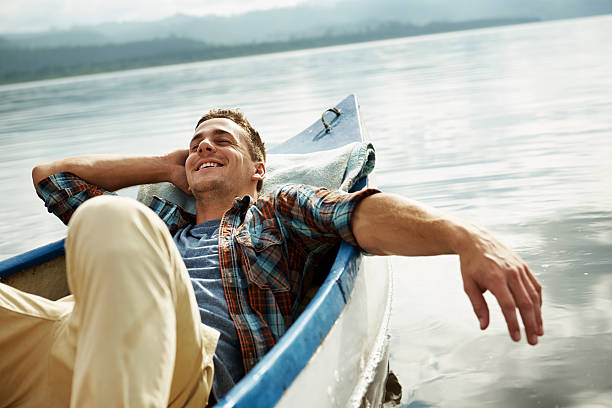 Taking a day off from his hectic lifestyle An attractive young man relaxing and daydreaming in a canoe man reclining stock pictures, royalty-free photos & images