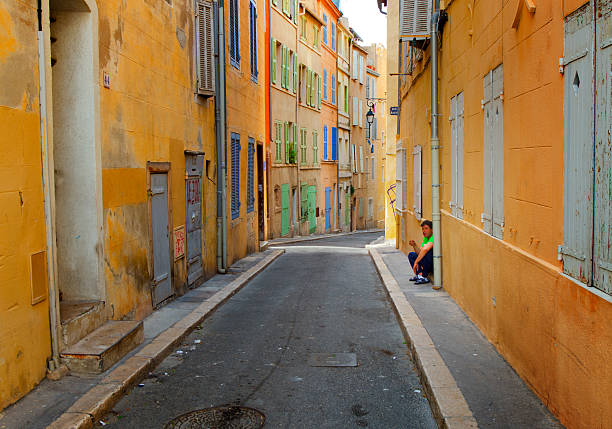 Man smoking in Panier Marseille France Marseille, France - May 22, 2014: A smoking man crouching and leaning to a wall on an alley in the historical Panier district of Marseille.  marseille panier stock pictures, royalty-free photos & images