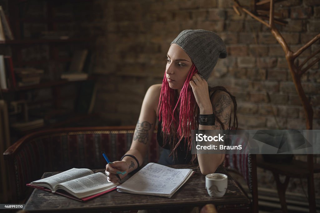 Pensive hipster student studying and looking away. Young woman with dreadlocks sitting in a cafe and thinking what to write. 2015 Stock Photo