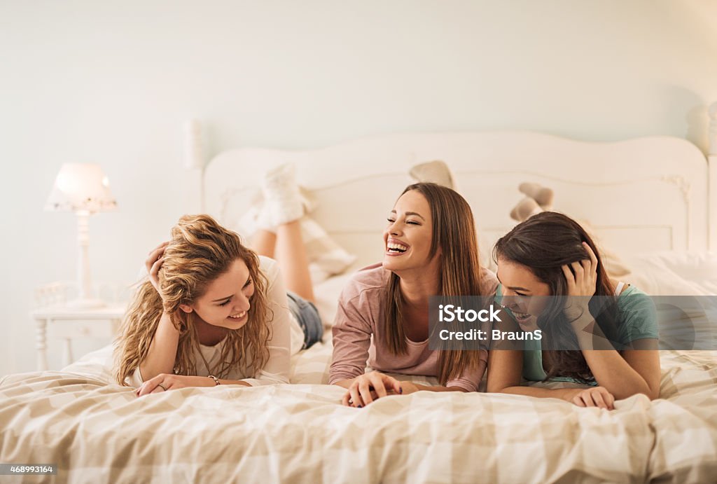 Women having fun in bedroom while talking to each other. Three cheerful women enjoying together in bedroom and communicating. Girls' Night In Stock Photo
