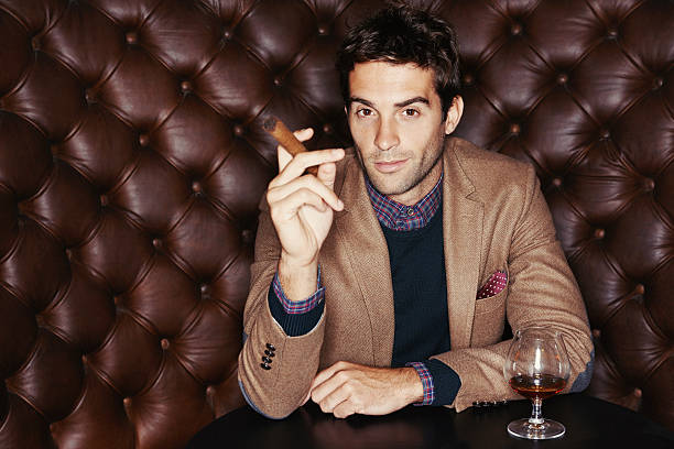 I like the finer things in life Portrait of a handsome young man drinking and smoking a cigar in a club man cigar stock pictures, royalty-free photos & images