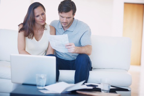 A young couple discussing their home finances and inspecting bills while sitting together in their living room