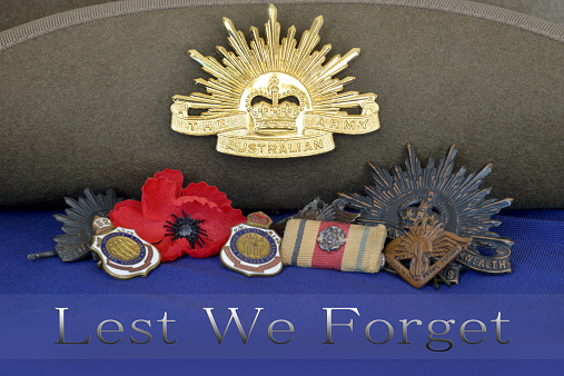 Close up of war medals resting against a slouch hat including a poppy sitting on a blue flag with the words, Lest We Forget
