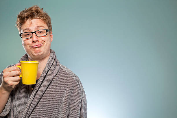 Nerdy guy drinking coffee Nerdy guy with a tea or coffee and looking blissful and smug in the early hours of the morning. He's wearing a dressing gown and is still in his pyjamas having just gotten out of bed. slapstick comedy stock pictures, royalty-free photos & images