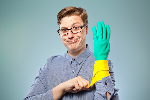 A nerdy guy looking at camera putting a rubber glove on getting ready to clean. He's feeling confident and ready to get the job done. Time to clean up!