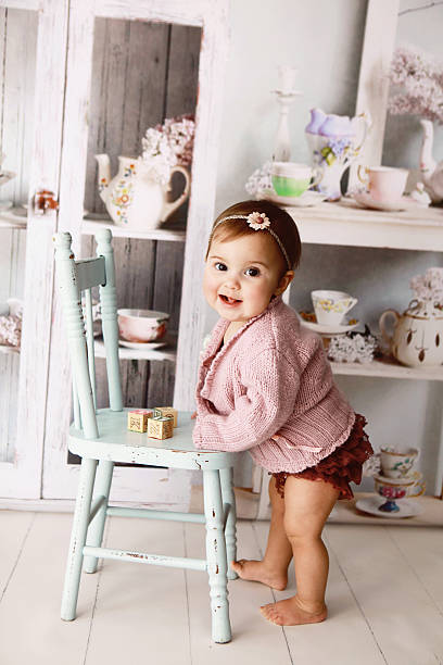 Baby girl standing while holding a blue wooden chair stock photo