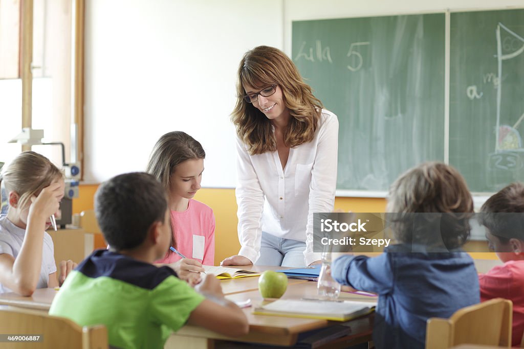 Teacher In Classroom Elementary classroom setting. Focus on teacher and chalkboard. Adult Stock Photo
