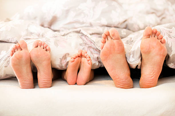 Family of feet Three pairs of feet - two parent family with one child in bed under blanket. Caucasian people, unrecognizable. bed human foot couple two parent family stock pictures, royalty-free photos & images
