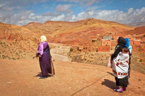 Ait Ouglif, Morocco - March 30th, 2012: Women in traditional clothes, one with child on her back looking at the village in a gorge of the Dadès River.