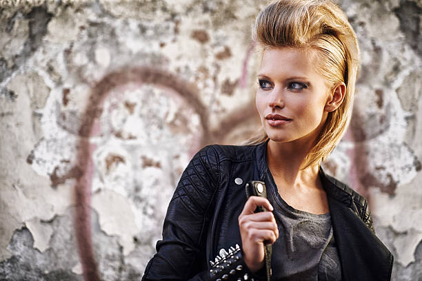 An edgy young woman holding the collar of her leather jacket