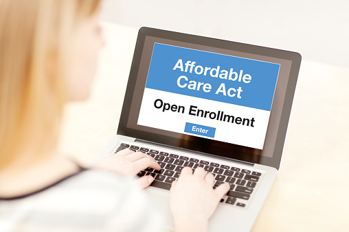 A woman using a laptop computer and the internet web service, she is in the process of signing up and joining the Affordable Care Act Obamacare in the United States in the open enrollment for her healthcare insurance plan. Photographed close-up in a horizontal format.