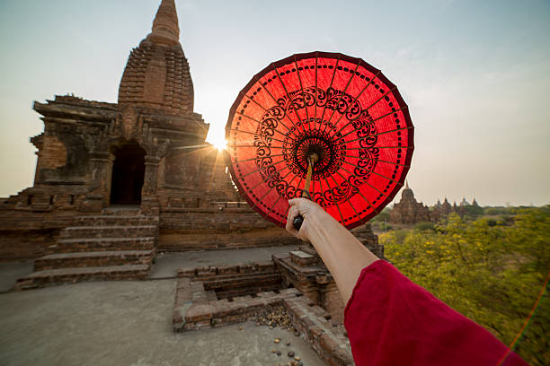 Young monk at the Bagan temples holding a red parasol directed to the sunset, umbrella covering the sun making sunbeam.