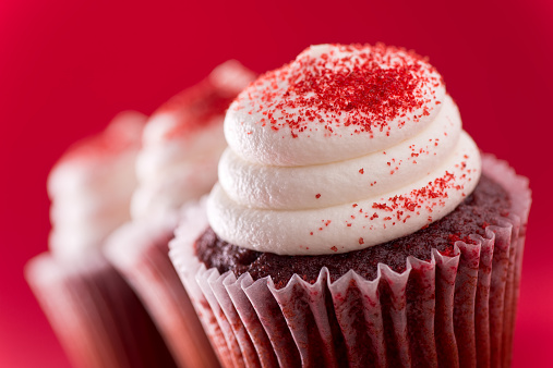 Three delicious red velvet cupcakes against a red background.