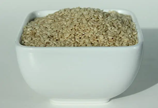 Photo showing a pile of tiny sesame seeds, piled high in a small square white dish.  Sesame seeds are often sprinkled onto the top of burger buns for an added crunch, while they are also used as an ingredient in Asian cuisine.