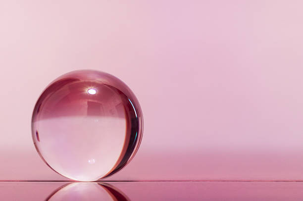 Glass transparent ball on light pink background and mirror surface
