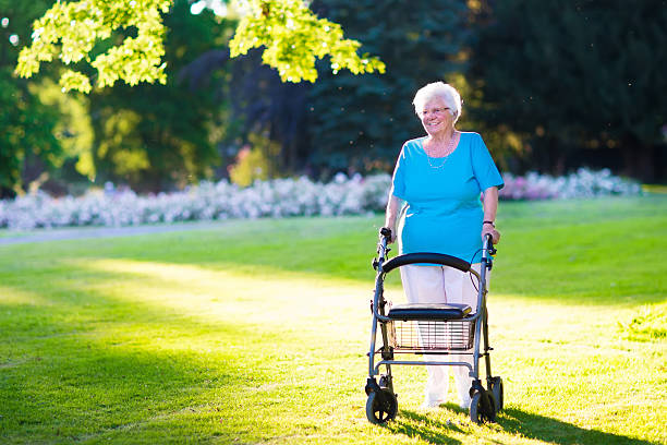 Happy senior handicapped lady with a walking disability enjoying a walk in a sunny park pushing her walker or wheel chair, aid and support during retirement concept.