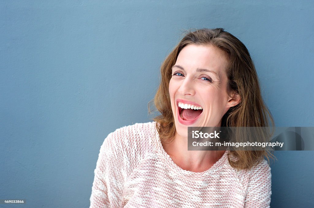 Happy beautiful fresh mid adult woman laughing Close up portrait of a happy beautiful fresh mid adult woman laughing on blue background Women Stock Photo