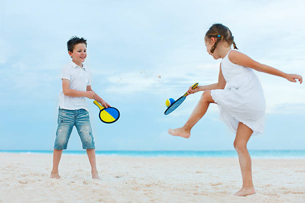 Happy girls playing to volleyball in the sea shore at sunset. Young people having fun on summer vacation. Travel, party and friendship concept. Image