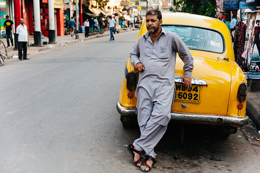 Kolkata, India - March 4, 2014: A taxi driver leans back against his vintage yellow british taxi cab in the streets of Kolkata, India