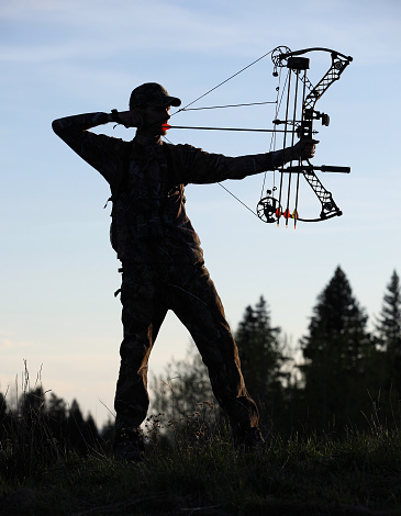 silhouette of a modern bowhunter drawing bow back in woods