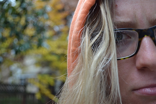 Close up of irritated, annoyed teenaged girl with glasses and orange hoodie.