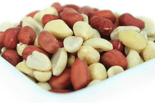 Photo showing a heap of redskin peanuts, which are piled high in a small square dish, ready to be enjoyed as an afternoon snack, being healthier than their salted or dry roasted alternatives.  While most people refer to peanuts as being 'nuts', in fact they belong to the legume family, growing in pods below the ground.