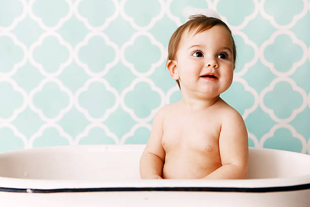 Baby in Bathtub A baby takes a bath in a little antique tub. She has soap suds on top of her head. Copy space in vintage wallpaper. girls bath stock pictures, royalty-free photos & images