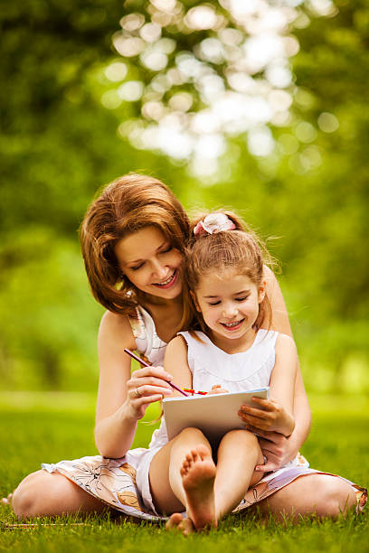 Mother and daughter drawing on grass in park stock photo