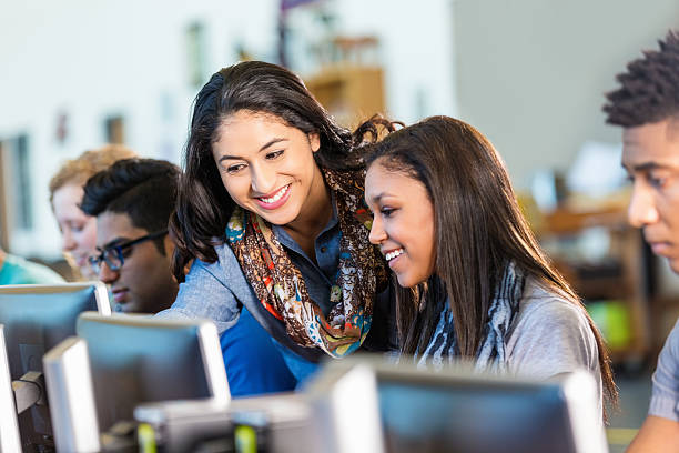 Happy Hispanic teacher assisting high school students with computers. Production Tool Ref #12 computer lab stock pictures, royalty-free photos & images