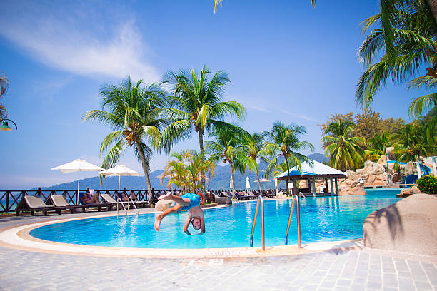 Happy child, active school age boy, jumping into a swimming pool having fun during summer vacation in a beautiful tropical resort