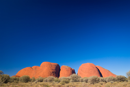 Kata Tjuta, Australia - July 6, 2007: The amazing red Kata Tjuta (Olgas) sandstone rock formations in Uluru-Kata Tjuta National Park in outback Australia stand out strongly against a brilliant blue afternoon sky. Grey-toned acacia scrubland fills the foreground.