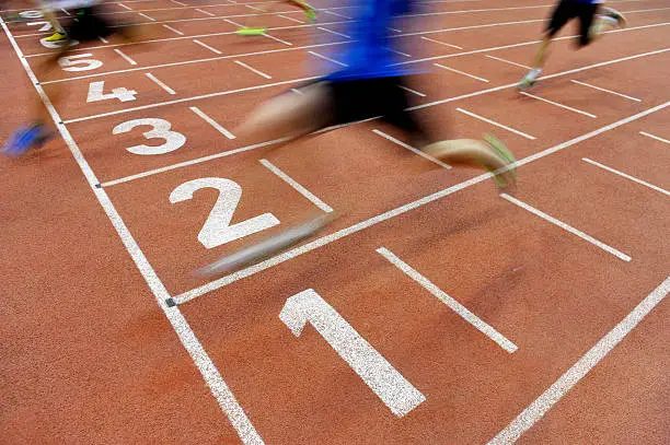 Blurred athletes by a slow camera shutter speed are crossing the finish line after sprint track