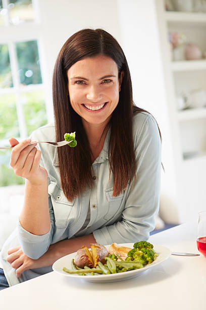 Portrait Of Woman Eating Healthy Meal In Kitchen Portrait Of Woman Eating Healthy Meal In Kitchen Smiling To Camera smiling potato stock pictures, royalty-free photos & images