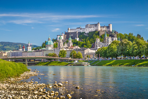 The view over Salzburg, Austria on a bright spring evening.  In the foreground are church spires of the Cathedral and the Hohensalzburg fortress with snow covered mountains of the Alps.