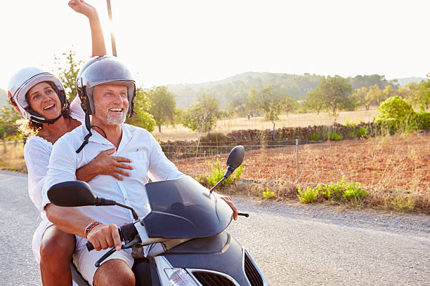 Mature Couple Riding Motor Scooter Along Country Road Mature Couple Riding Motor Scooter Along Country Road moped stock pictures, royalty-free photos & images