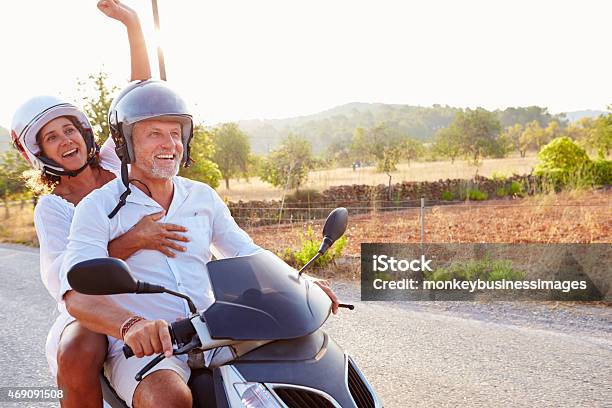 Mature Couple Riding Motor Scooter Along Country Road Stock Photo - Download Image Now