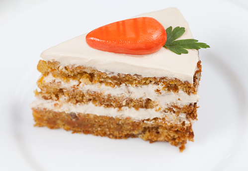 Slice of homemade tasty carrot sponge cake with pastry cream and little orange carrots on white background