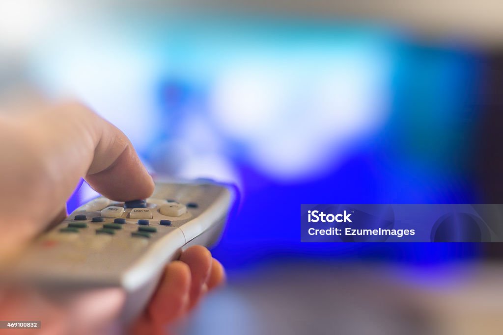 Watching Television Close up of remote in hand with shallow depth of field during television watching Advertisement Stock Photo