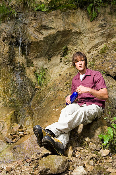 istock Young man sitting by waterfall, looking away 469101220
