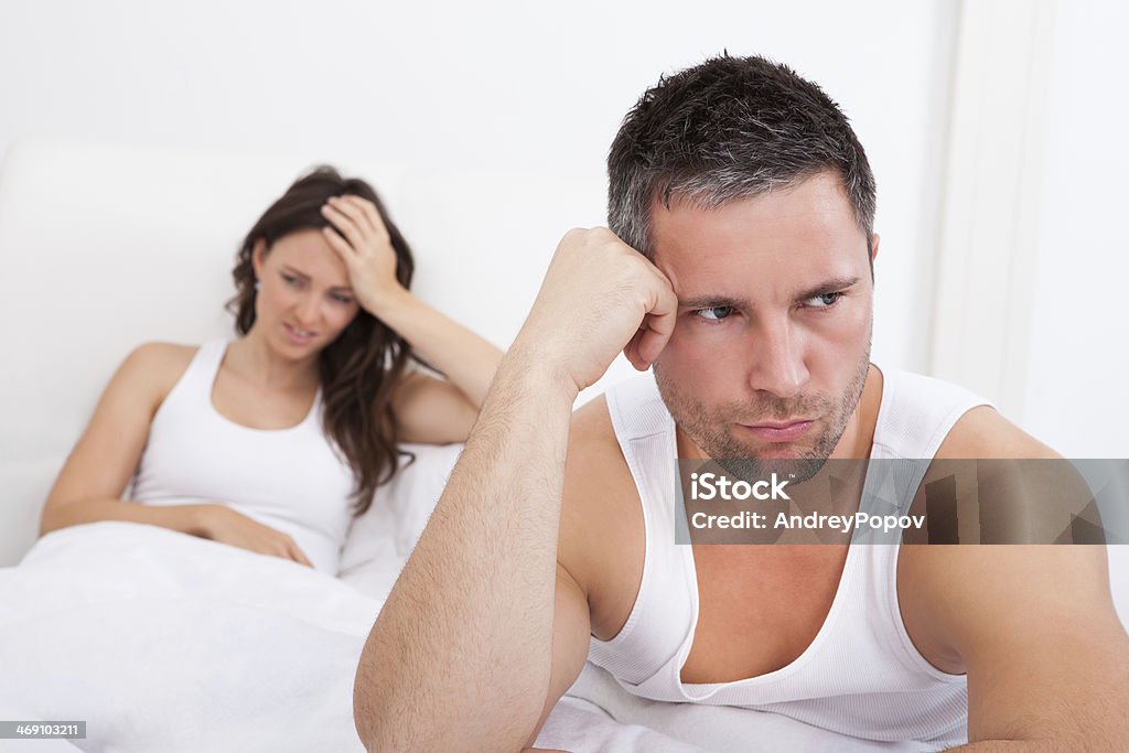 Frustrated Couple On Bed Frustrated Man Sitting On Bed In Front Of Young Woman Accidents and Disasters Stock Photo