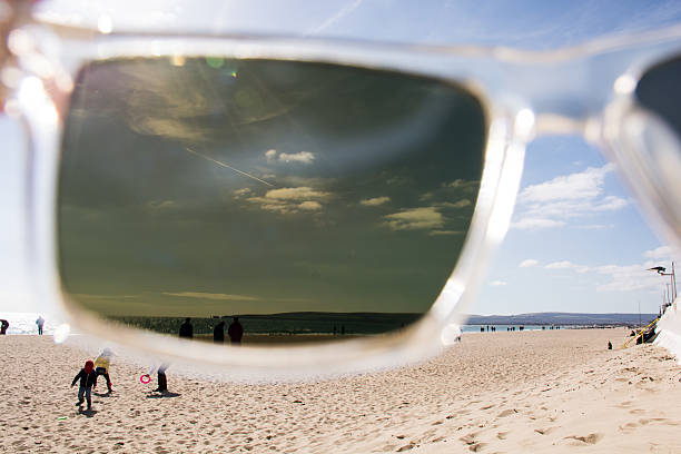 A view of a British beach looking through polarised sunglasses, a family plays in the foreground with the ocean and hills in the background
