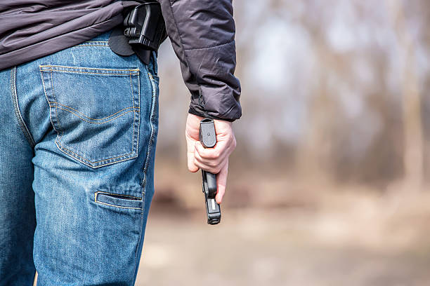 Close-Up of Man Holding .45 Caliber Handgun Rear view close-up of a man holding a .45 caliber handgun. The gun holster is visible at the side of his waist. This man has a conceal and carry license. Photo taken outdoors on a cool spring day. forty five caliber handgun stock pictures, royalty-free photos & images