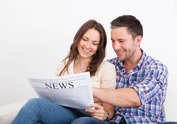 istock Happy Young Couple Sitting On Couch Reading Newspaper 469111825